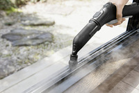 Hand using Kärcher steam cleaner on window frame, outdoors with blurred garden in background.