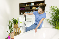 Person in blue shirt using a Kärcher high-pressure cleaner on a bathroom tap, surrounded by indoor plants and shelves with towels and baskets.