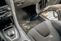 Person using a Kärcher vacuum cleaner to remove dirt from a car's floor mat, with visible debris and car interior details.