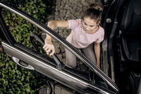 Person cleaning car interior with Kärcher vacuum on cobblestone driveway, wearing striped shirt and grey trousers.