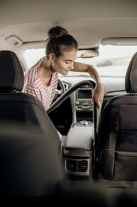Person cleaning car interior with vacuum, wearing a striped shirt, inside a vehicle with black seats and central console.