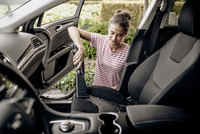 Person using a Kärcher vacuum cleaner to clean car interior, with open door and visible outdoor greenery.