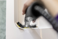 Hand using Kärcher steam cleaner on white surface corner.