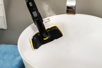 Kärcher steam cleaner head emitting steam inside a white sink, with a blue towel nearby.
