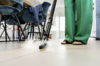 Person using a Kärcher steam cleaner on a tiled floor indoors, with steam visible. Green trousers and sandals are worn.