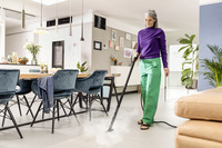 Person cleaning a modern living room floor with a Kärcher steam cleaner, surrounded by stylish furniture and indoor plants.