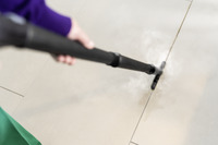 Person using a Kärcher steam cleaner on tiled floor, with steam visibly cleaning grout lines.