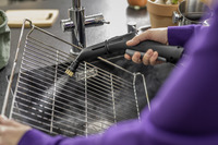 Hand cleaning a grill rack with a Kärcher steam cleaner in a kitchen setting.