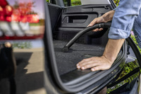 Person using a Kärcher vacuum cleaner to clean the boot of a car, with reflections visible on the car's exterior.