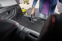 Person vacuuming car boot with Kärcher vacuum cleaner, outdoor setting with potted flowers in background.