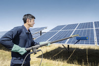 Person cleaning solar panels outdoors with a Kärcher cleaning tool, wearing green gloves, under a clear blue sky.