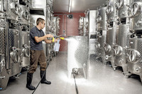 Person using Kärcher high-pressure cleaner to spray foam on a stainless steel tank in an industrial setting.