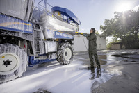 Person using Kärcher high-pressure cleaner on New Holland agricultural machine outdoors.