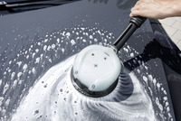 Hand using Kärcher surface cleaner on a car bonnet, creating swirling soap patterns.