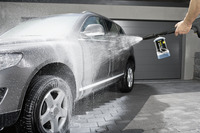 Grey SUV being cleaned with Kärcher high-pressure cleaner, spraying water and foam, parked on a driveway near a garage.