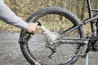 Hand sprays cleaner on muddy mountain bike gear outdoors.