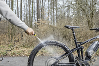 Person cleaning a muddy bicycle tyre with a Kärcher high-pressure cleaner in a forest setting.
