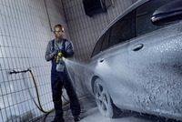 Person using Kärcher high-pressure cleaner to wash a car with foam in a tiled indoor setting.