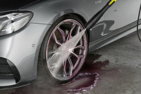 Silver car wheel being cleaned with Kärcher high-pressure cleaner, spraying water on the rim in a garage setting.