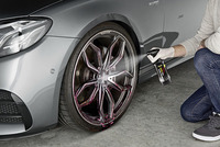 Person spraying Kärcher rim cleaner on a car wheel, wearing gloves, indoors on a concrete floor.