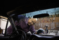 Person cleaning car interior with spray bottle and cloth in a garage, tools hanging on wall in background.