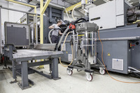 Industrial setting with a Kärcher vacuum cleaner on wheels near a large machine, a person working with hoses connected to the equipment.