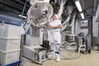 Worker in white uniform cleaning industrial mixer with Kärcher vacuum cleaner in a tiled factory setting.
